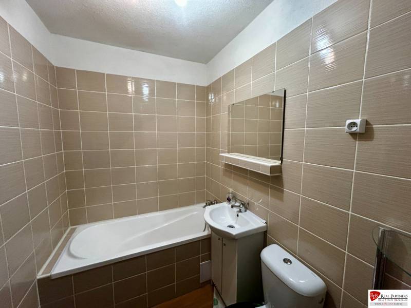Bathroom with a bathtub, sink, toilet, and tiles in a studio apartment.