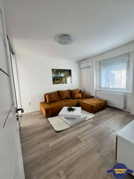A bright living room in a two-room apartment with a brown sofa and a table on a floor with a wooden decor.