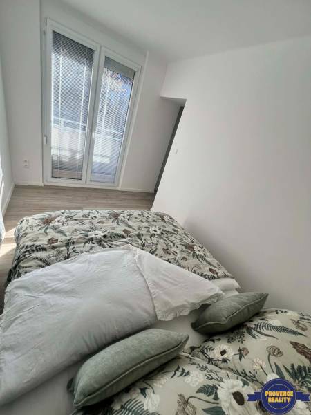Bright bedroom in a two-room apartment with decorative pillows and a wooden-patterned floor.