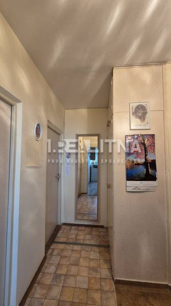 A hallway in a 2-room apartment with tiled flooring and a mirror on the wall.