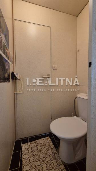 A bathroom in a 2-room apartment with black tiles and a floral patterned rug.