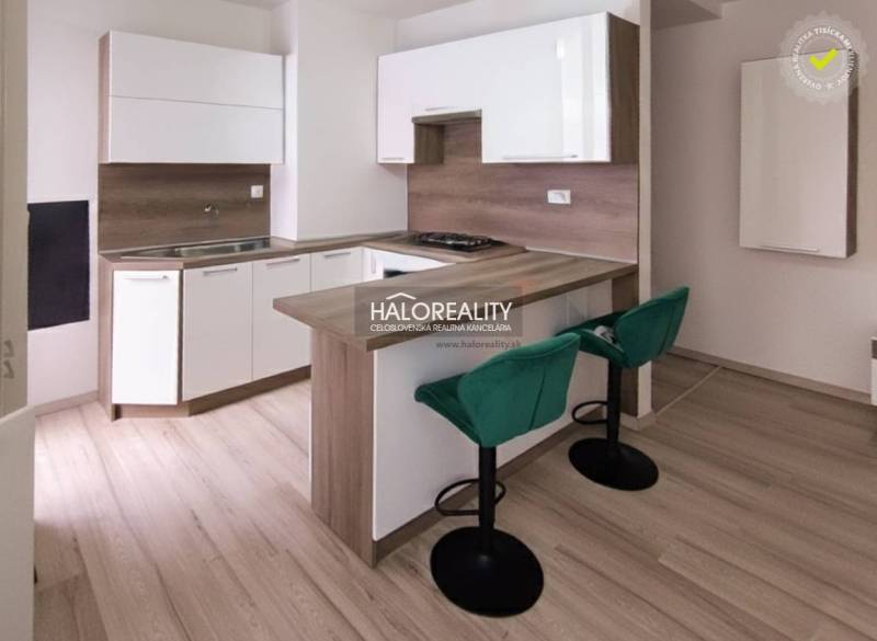 A kitchen in a 2-room apartment with a bar counter, green chairs, and a wooden decor floor.