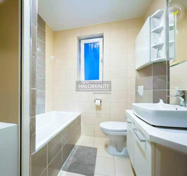 A bathroom with a bathtub and a sink in a 2-room apartment, featuring light-colored tiles.