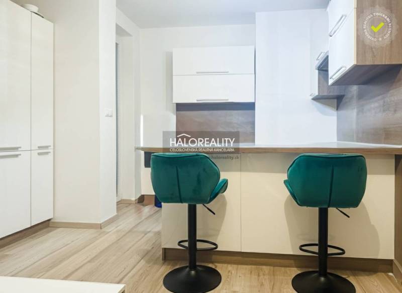 A kitchen in a 2-room apartment with turquoise chairs and a wooden decor floor.