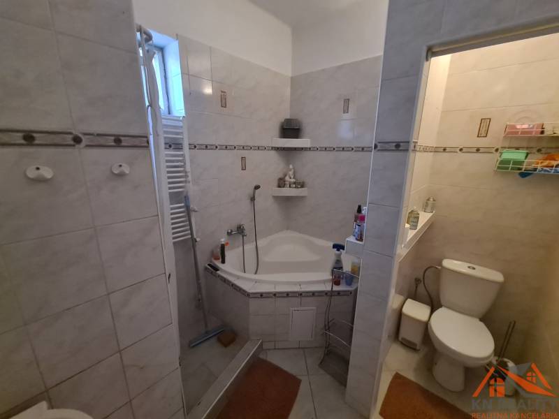 A bathroom in a family house with a bathtub and a separate toilet, tiled with light tiles.