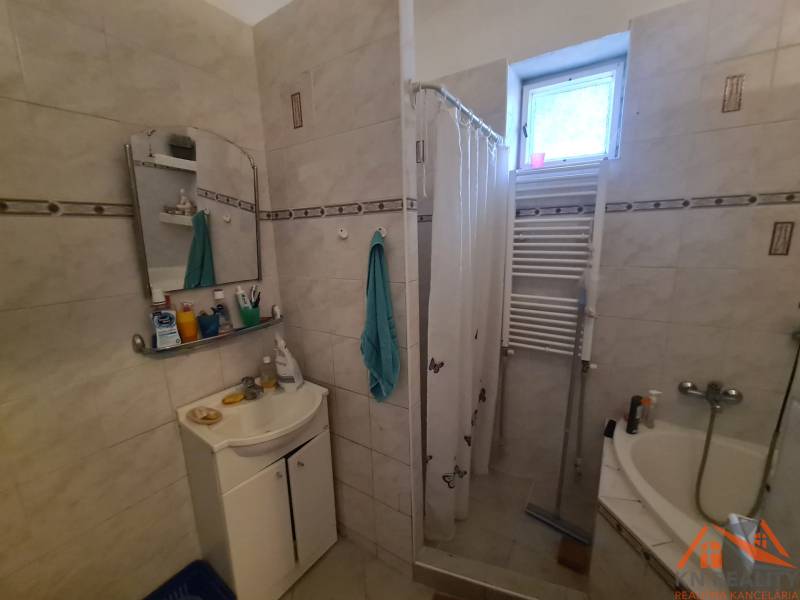 Bathroom in a family house, shower with a curtain, sink, mirror, and radiator.