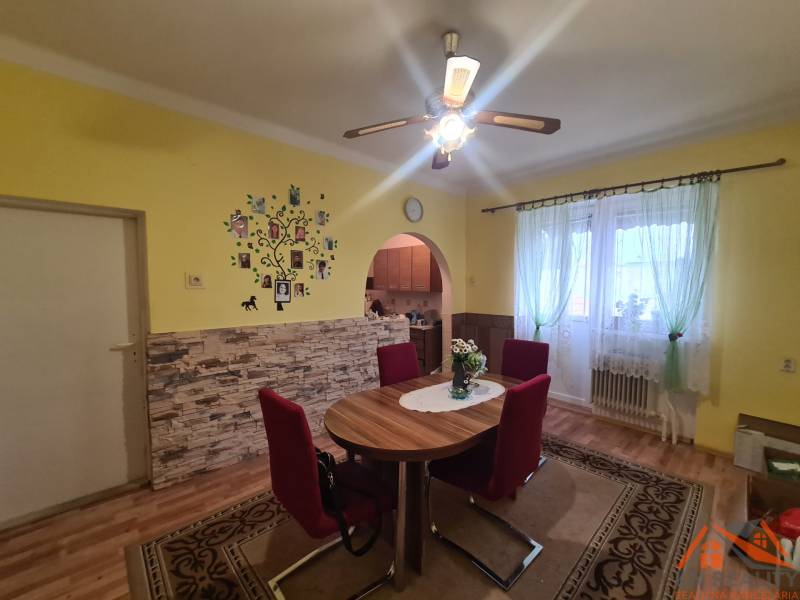 Dining room in a family house with a decorative wall, wood-patterned floor, and red chairs.