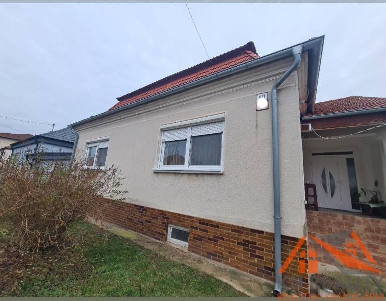 A family house in Hurbanovo with a light facade and a red roof, surrounded by bushes.