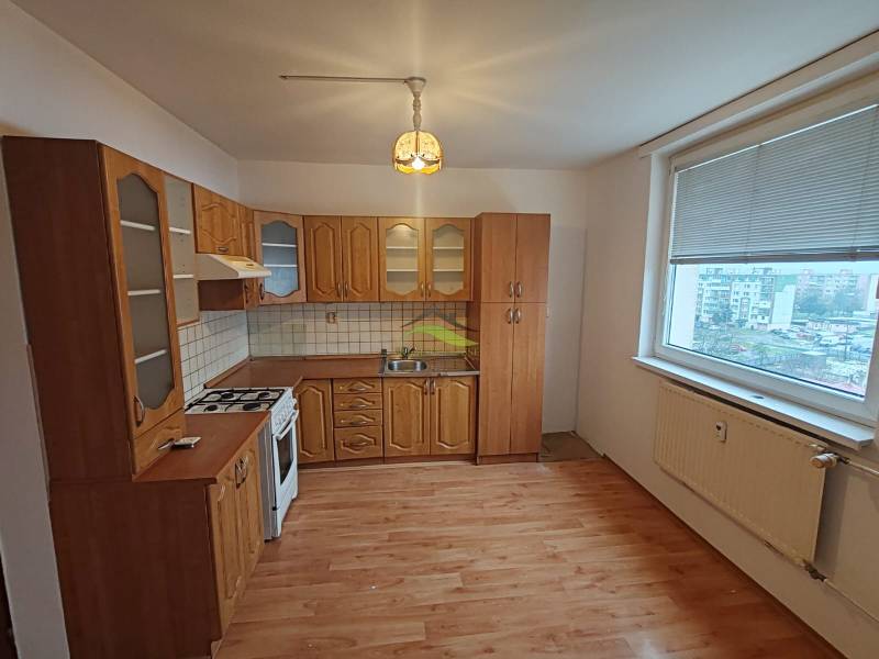 A kitchen in a 3-room apartment with a wooden decor floor and a large window.