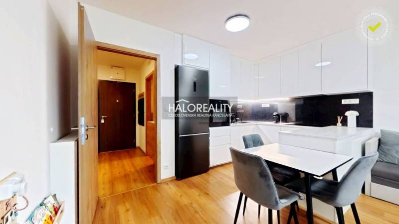 A kitchen in a 2-room apartment with a dining table, built-in kitchen unit, and a floor with a wood decor.