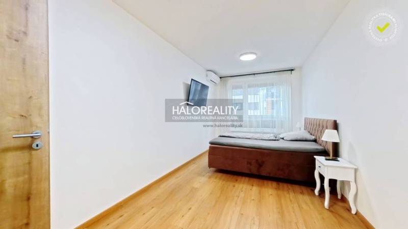 A bedroom in a two-room apartment with a bed, a nightstand, and a television, has a floor with a wood decor.