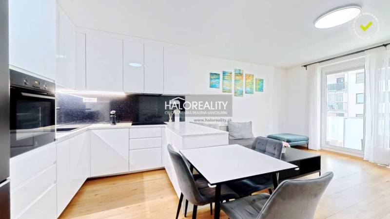 A kitchen in a 2-room apartment with white cabinets, a dining table, and a wooden decor floor.