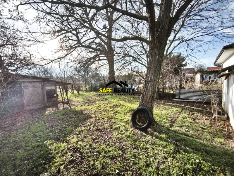 The garden of a family house in Lúčnica nad Žitavou with a lawn, trees, and a simple gazebo structure.