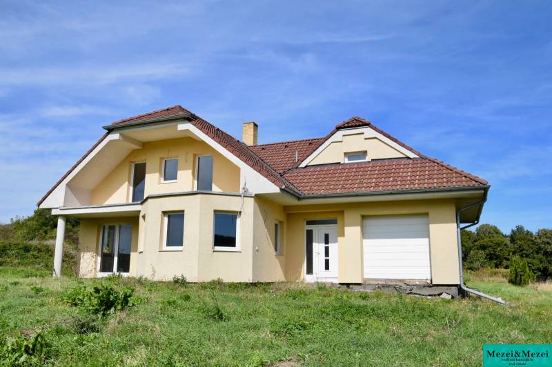 A family house in Buková with a sloped roof, light facade, and garage, surrounded by greenery.
