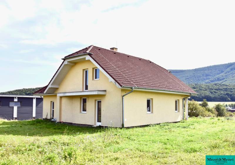 A family house in Buková with a red roof and a grass-covered yard, surrounded by nature.