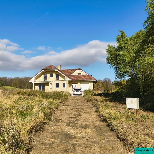 A family house in Buková with an access road, a car, and surrounding nature under a blue sky.