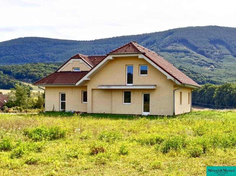A family house in Buková with a red roof surrounded by green hills in the background.