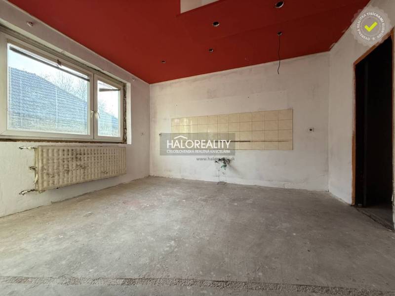 An empty room with a concrete floor in a family house with a red ceiling and a radiator.
