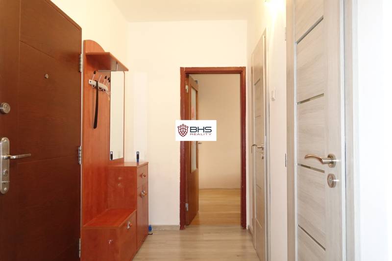 A hallway in a 3-room apartment with a wooden decor floor and light-colored furniture.