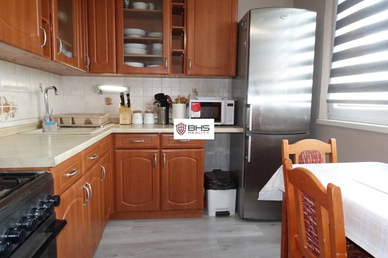 A kitchen with wooden decor, a stove, a refrigerator, and a dining table in a 3-room apartment.