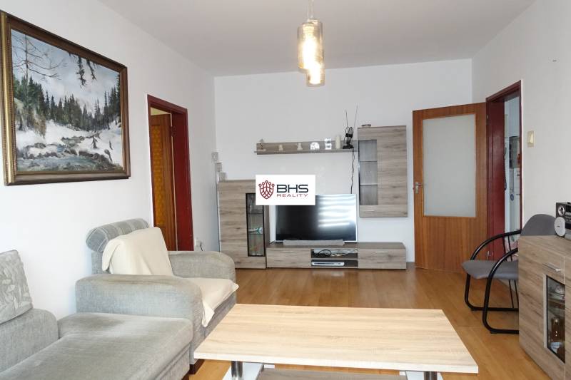 Living room of a 3-room apartment with a comfortable sofa, furniture with a wooden decor, and a television.