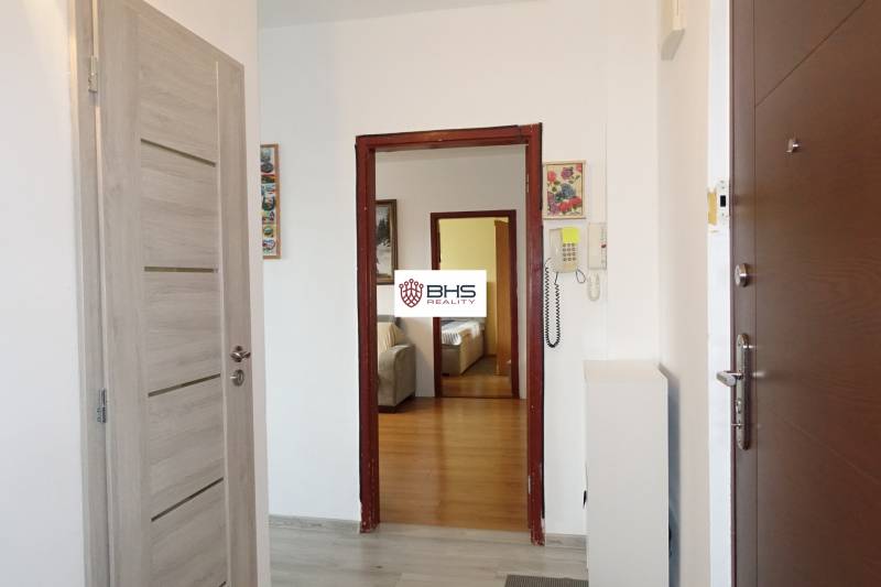 A hallway in a 3-room apartment with a wood-patterned floor and an intercom.