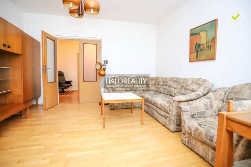 Living room of a three-room apartment with a sofa, table, and wooden decor flooring.