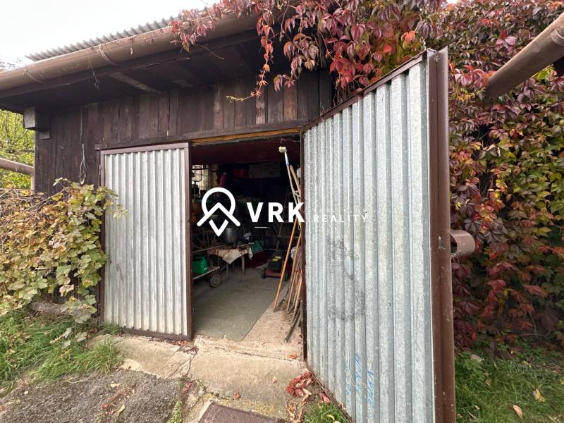Open metal garage door at a family house in Kalša, surrounded by lush vegetation.