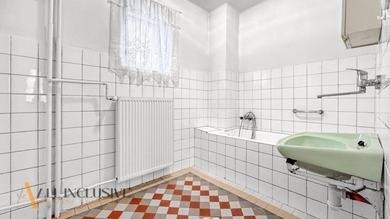 A bathroom in a family house with a bathtub, a green sink, and tiles on the floor.