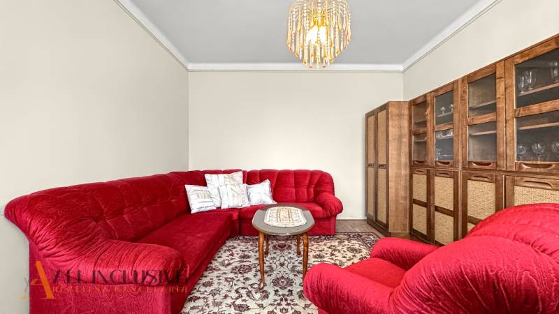 Red sofa set, table, display cabinet, and chandelier in a family house on a floor with a wooden decor.