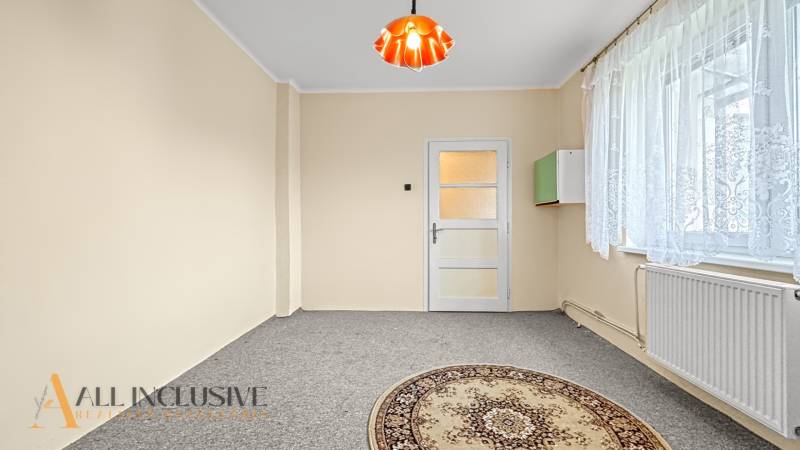 A bright room in a family house with a carpet and a window with a lace curtain.