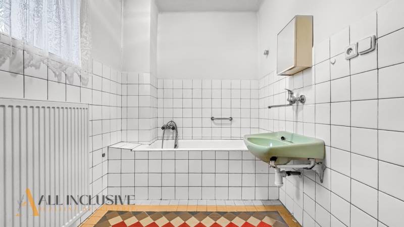 Bathroom in a family house with a rectangular bathtub, green sink, and striking tiles.