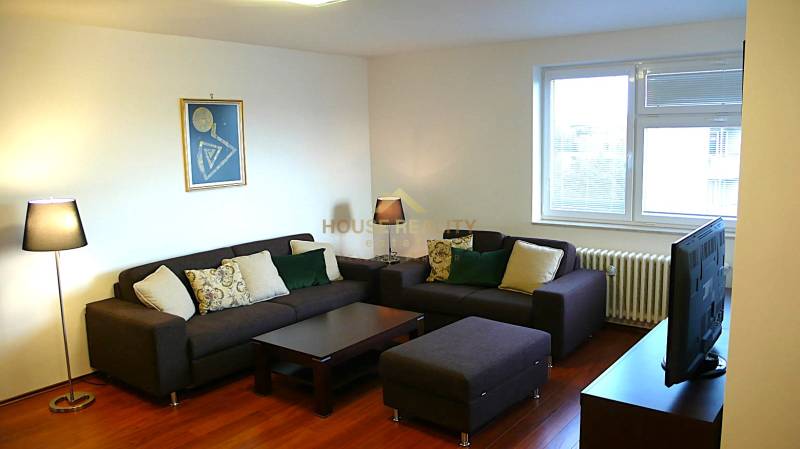Living room in a 4-room apartment with sofas, TV, and wood-patterned flooring.