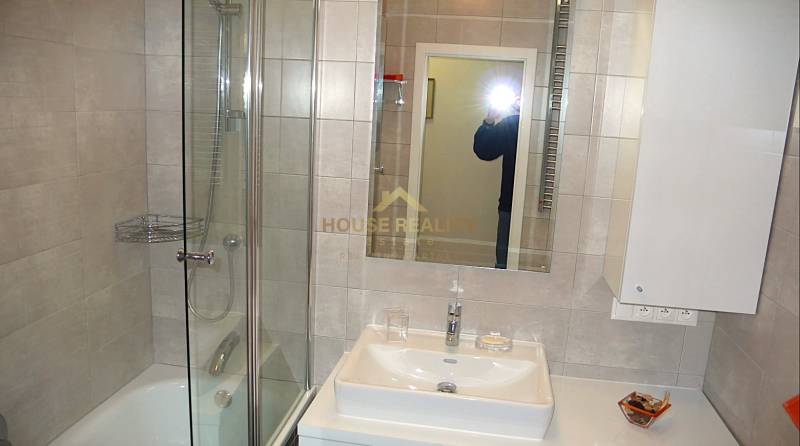 A bathroom with a shower, mirror, and sink in a 4-room apartment.