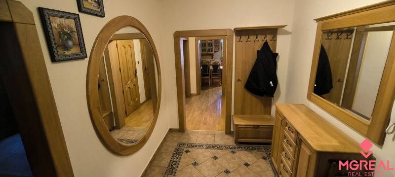 A hallway with a wooden decor floor, a mirror, and stylish furniture in a 3-room apartment.