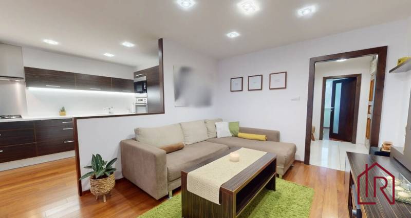 Living room in a three-room apartment with a wood-patterned floor and a comfortable sofa set.