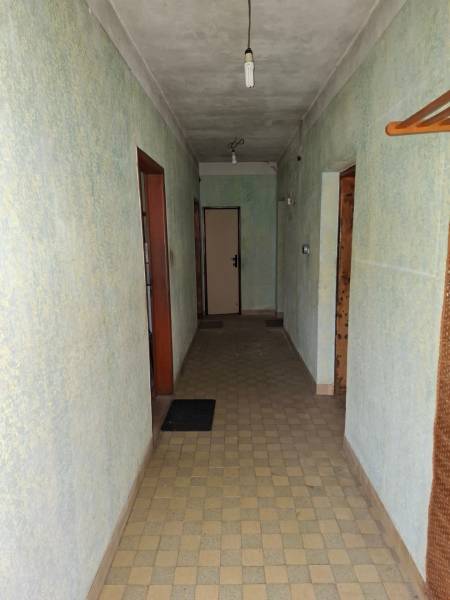 A hallway in a family house with light green walls, tiles, and simple lighting.
