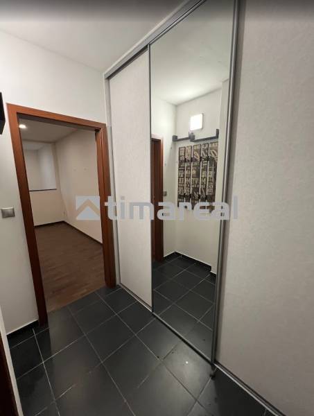 A hallway with tiled flooring and a mirrored wardrobe, leading to a room with wood-patterned flooring.