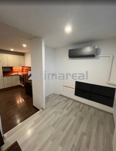 Interior of a 1-room apartment with air conditioning, built-in kitchen, and wooden decor flooring.