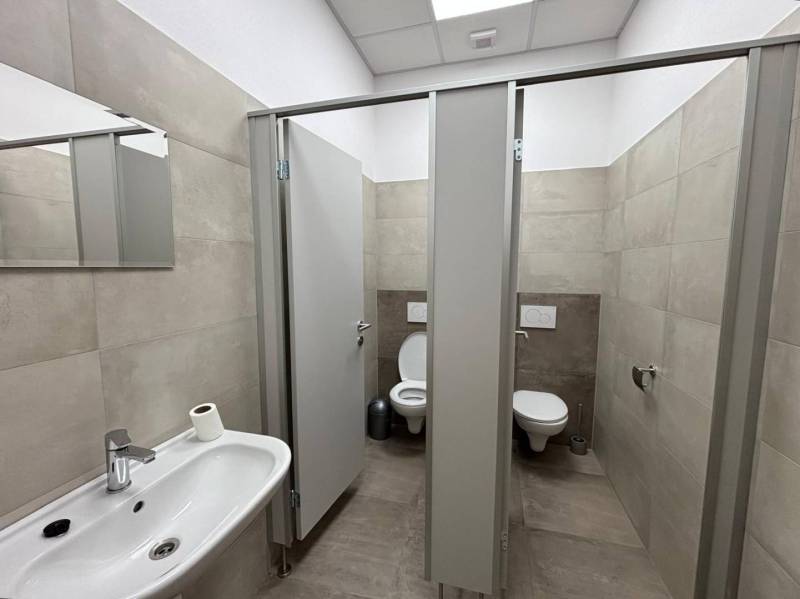 Office restrooms with a sink and stalls, floor with wood decor.