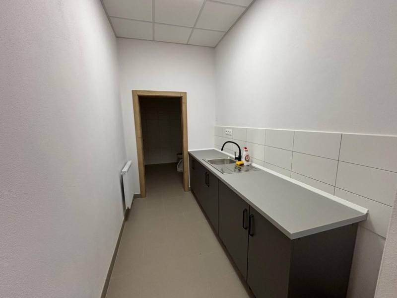 A narrow office with a kitchenette, gray tiles, and a sink.