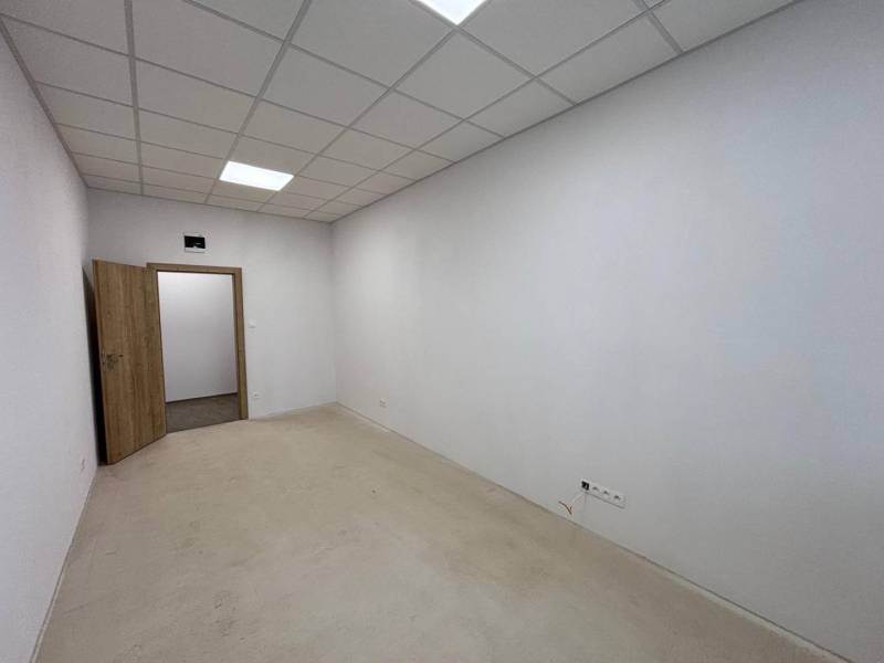 Interior of an office with white walls, a suspended ceiling, and open doors.