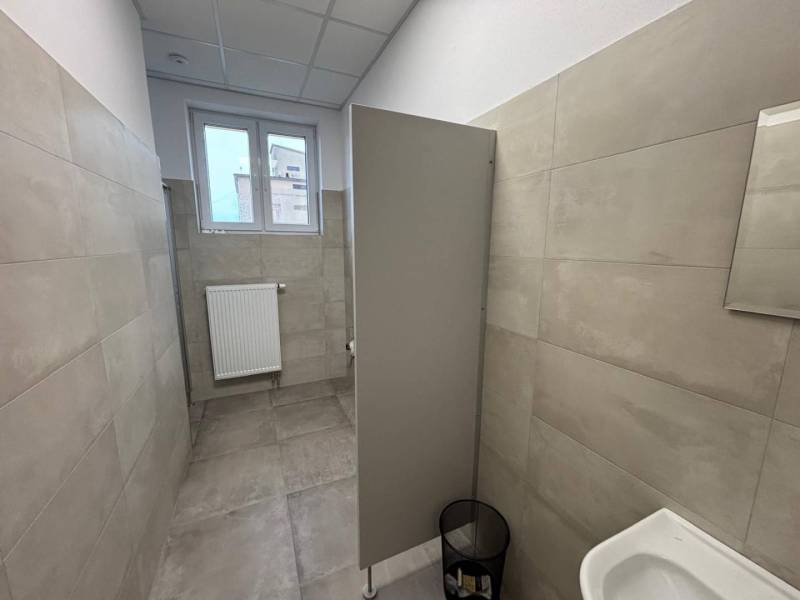 Offices with gray paneling and a toilet, with a small window and a ribbed radiator.