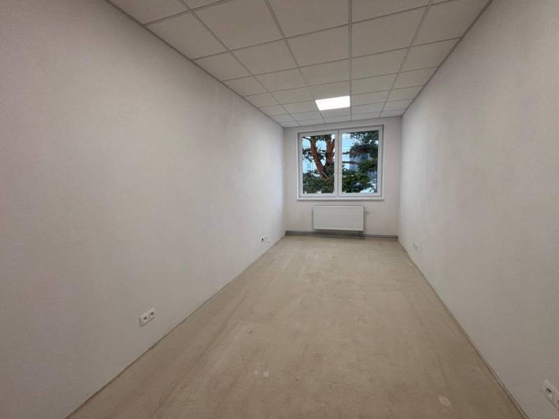 A white room with a window, radiator, and a floor with a wooden decor in the offices.