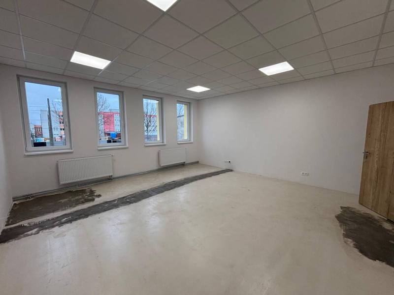 Empty offices with white walls, ceiling lighting, and wood-patterned flooring.