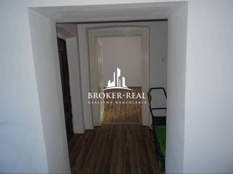 A hallway of a family house with a wooden decor floor and a view into another room.