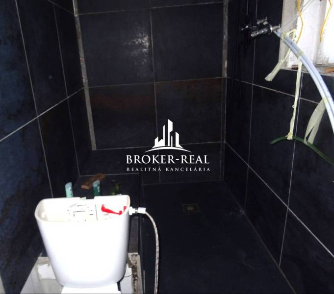 A bathroom with dark tiles and a toilet in a family house.