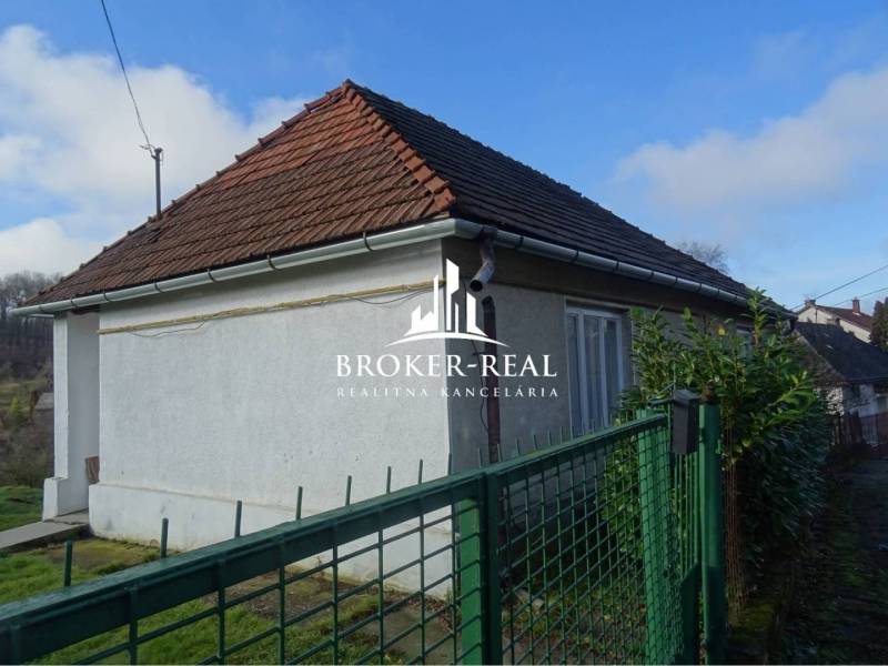 A family house in Rudabánya with a white facade and a sloped roof behind a green fence.