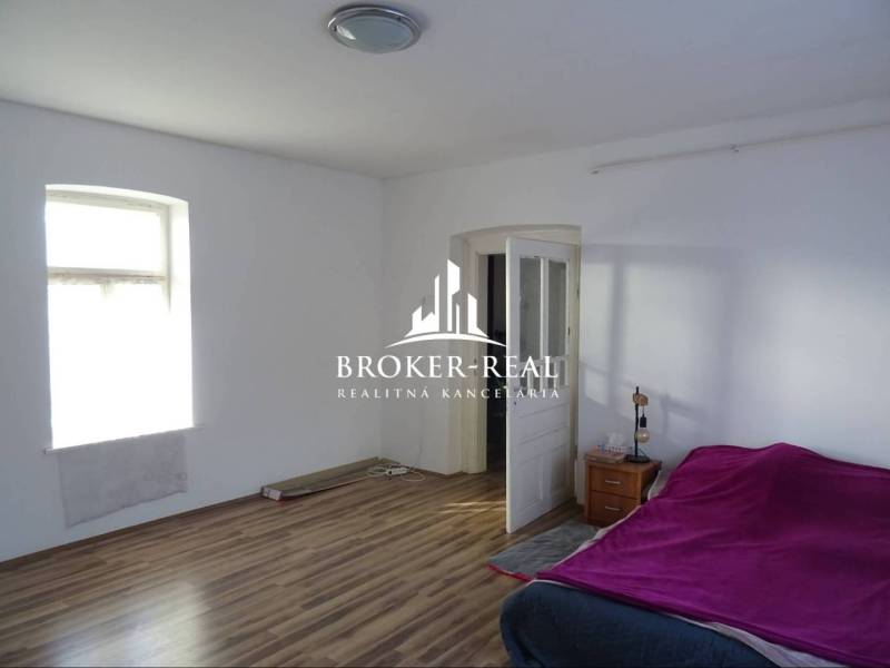 A room with a bed, a window, a floor with a wooden decor, a nightstand, and open doors.