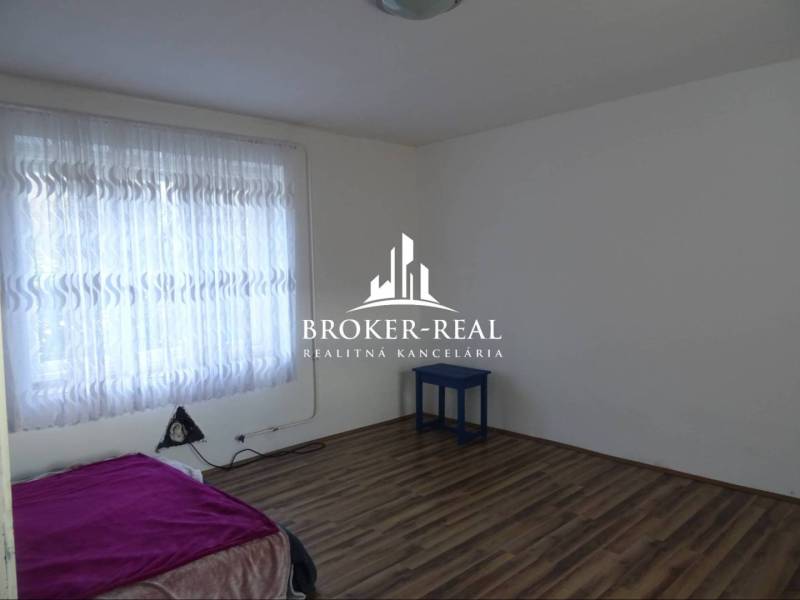 A room with a bed, curtains, and a wooden decor floor in a family house.